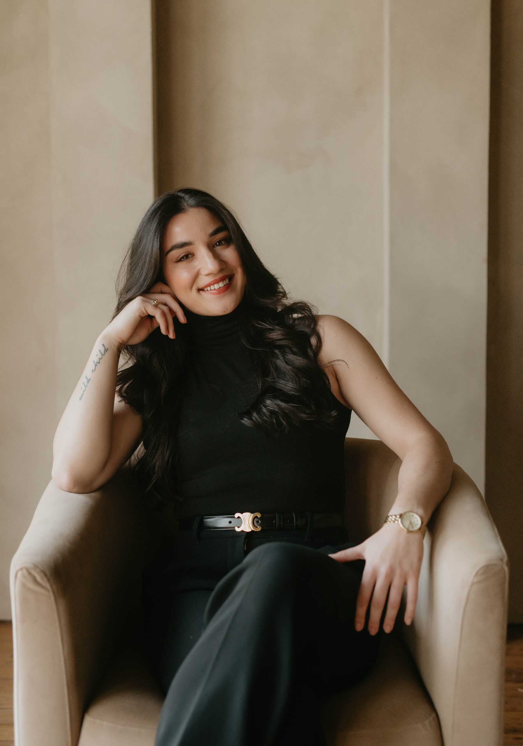 Woman with dark brown hair, wearing all black, sitting in a chair with head resting on hand.