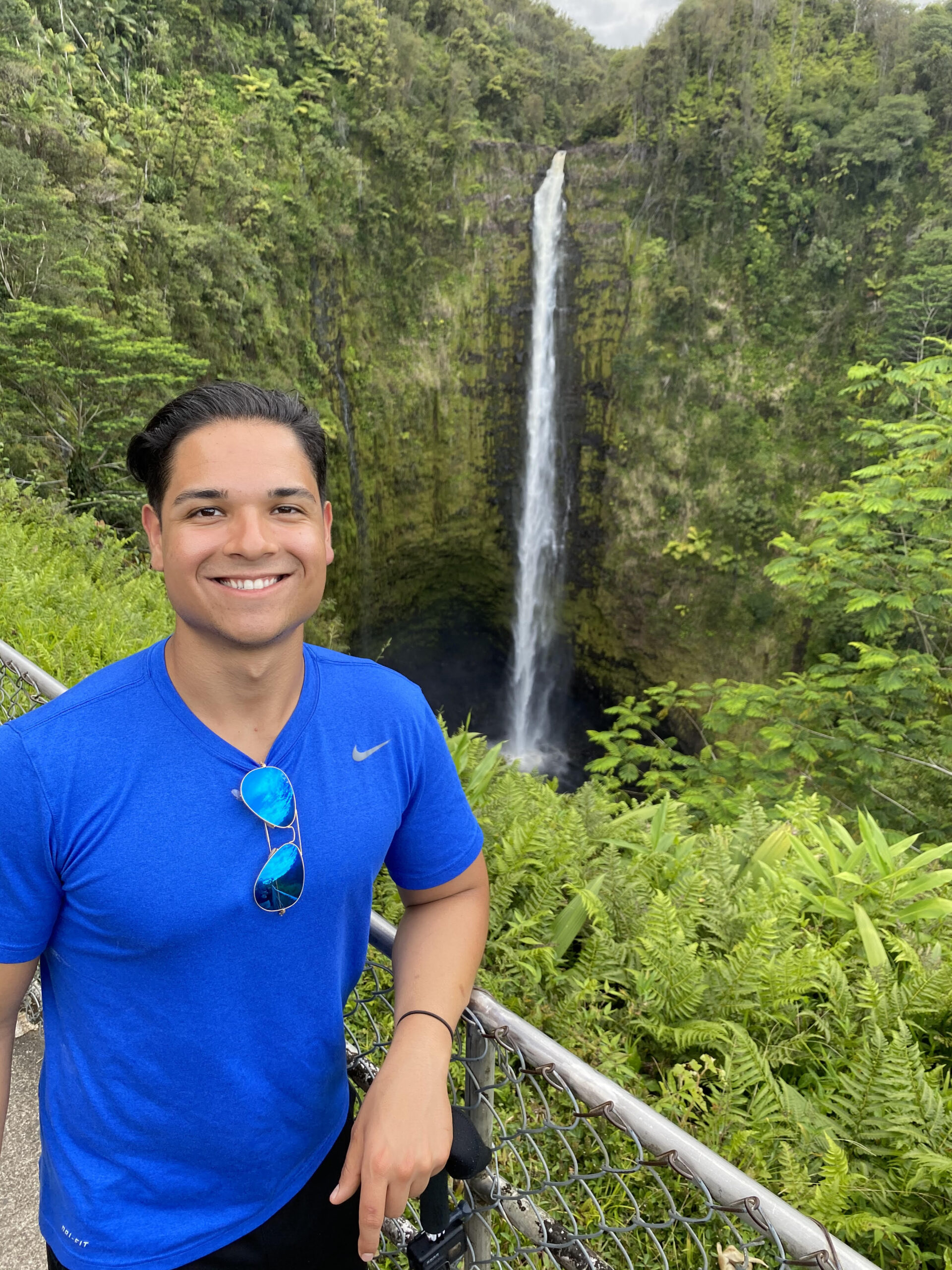 Man with brown hair wearing a blue shirt and standing by a waterfall